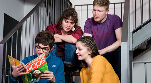 Vier junge Menschen sitzen auf einer Treppe und schauen in eine Broschre.