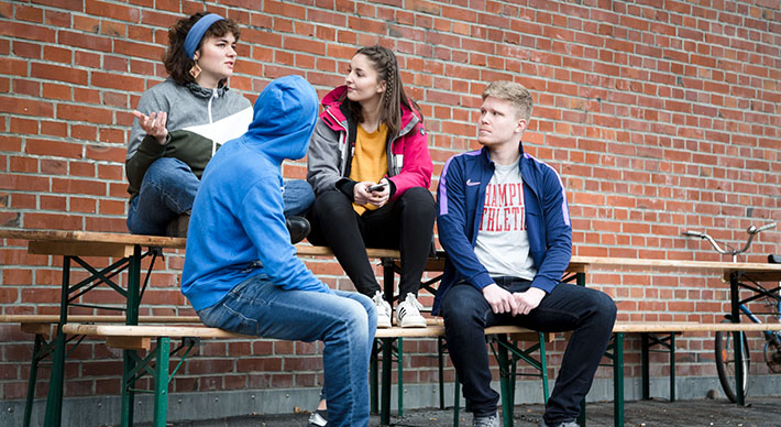 Vier junge Leute, zwei sitzen auf einem Tisch, zwei auf einer Bank davor.