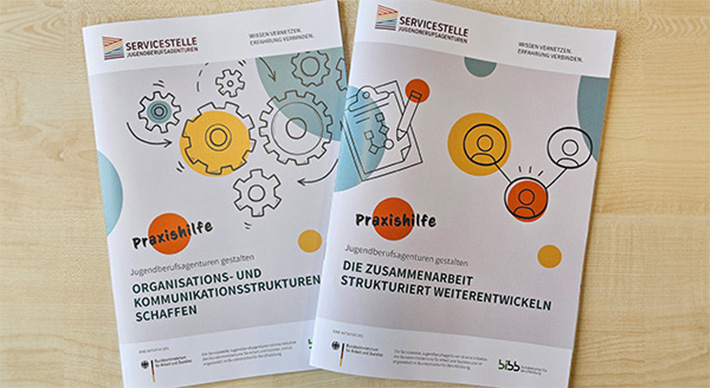 Je ein Druckexemplar der ersten beiden Praxishilfen-Ausgaben auf einem Tisch angeordnet