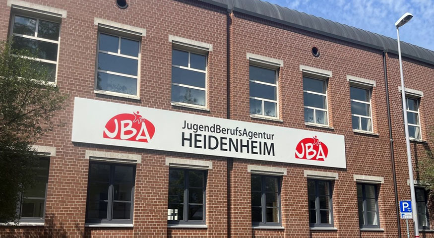 Außenansicht eines Gebäudes. Zwei Fensterreihen, dazwischen ein großes Schild mit der Aufschrift JugendBerufsAgentur Heidenheim.