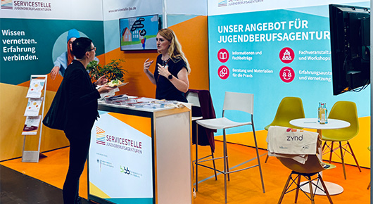 Der Messestand der Servicestelle mit zwei Personen