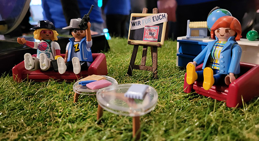 Lego-Modell mit Figuren in Sitzgruppe sowie Logo der JBA Essen und Text "Wir f�r euch"