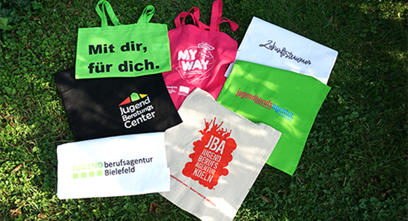 Mehrere Baumwolltaschen mit Logoaufdruck verschiedener Jugendberufsagenturen