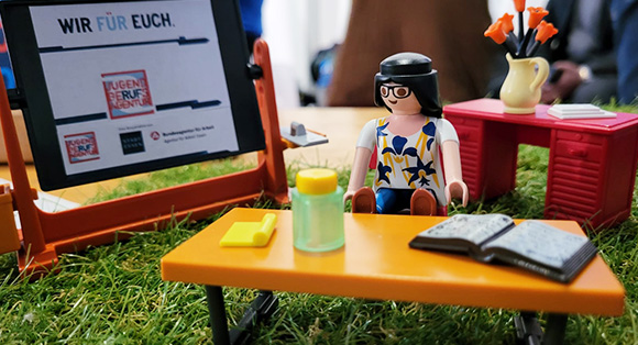 Lego-Modell mit Figur an Schreibtisch sowie Wandtafel mit Logo der JBA Essen und Text "Wir f�r euch"