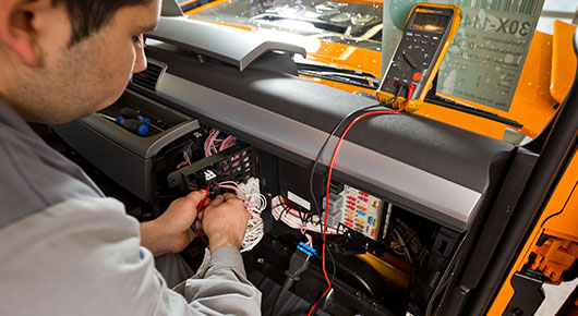 In einem LKW prüft ein Mann die Elektrik des Fahrzeugs mit einem Diagnosegerät. In einem LKW prüft ein Mann die Elektrik des Fahrzeugs mit einem Diagnosegerät.