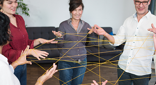 Eine Menschengruppe steht im Kreis und spannt ein Fadennetz zwischen sich.