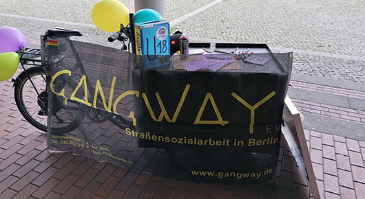 Ein Lastenrad mit Gangway-Banner lehnt an einem Laternenpfahl.