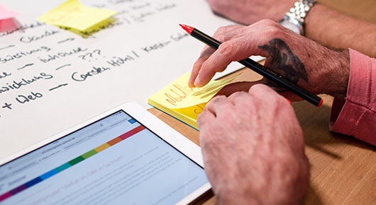 Hände, die einen Stift halten und Notizzettel sowie weitere Planungsunterlagen Hände, die einen Stift halten und Notizzettel sowie weitere Planungsunterlagen