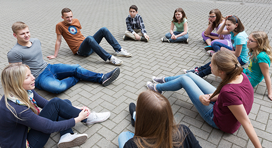 Eine Gruppe junger Menschen sitzt im Kreis auf dem Boden.
