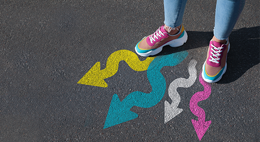 Eine Person in Turnschuhen, von denen vier auf den Asphalt gemalte Pfeile ausgehen